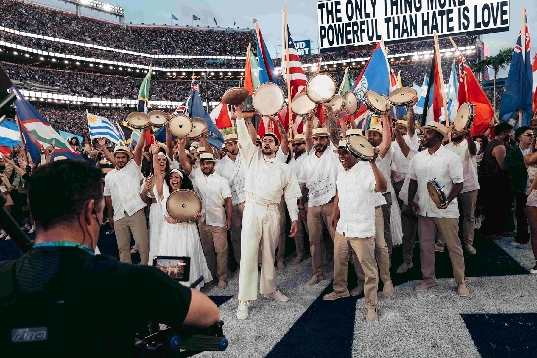 Bad Bunny SuperBowl - crowd of Latine people holding up drums and flags of all nations of the Americas