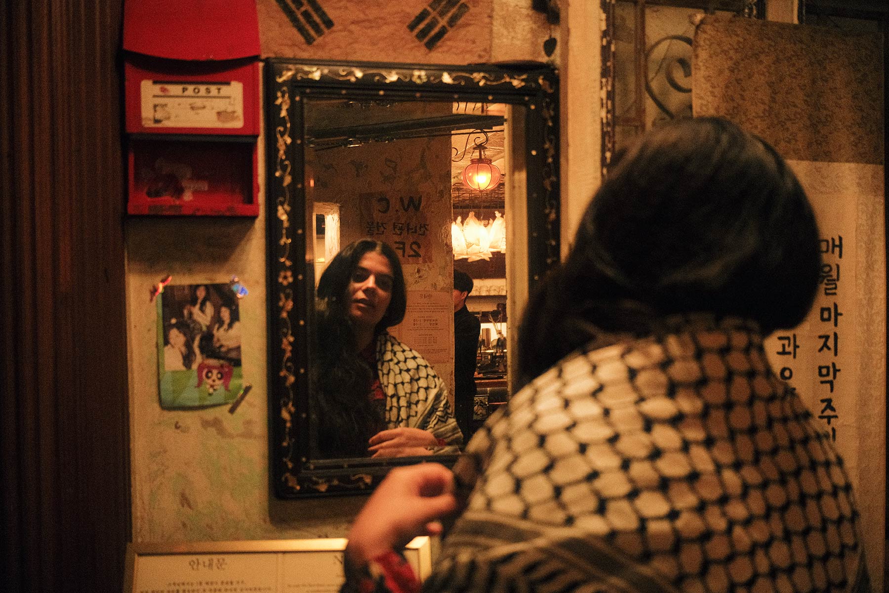 Nareman wearing a keffiyeh looking in the mirror of a bathroom in a restaurant in Seoul