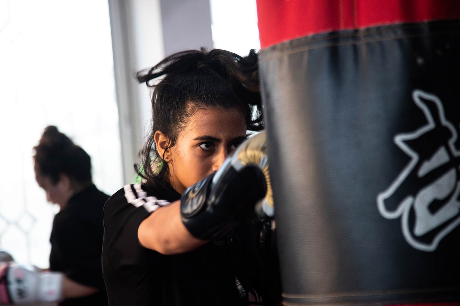 A dramatic shot of a girl punching a bag, gloves on, in the boxing gym