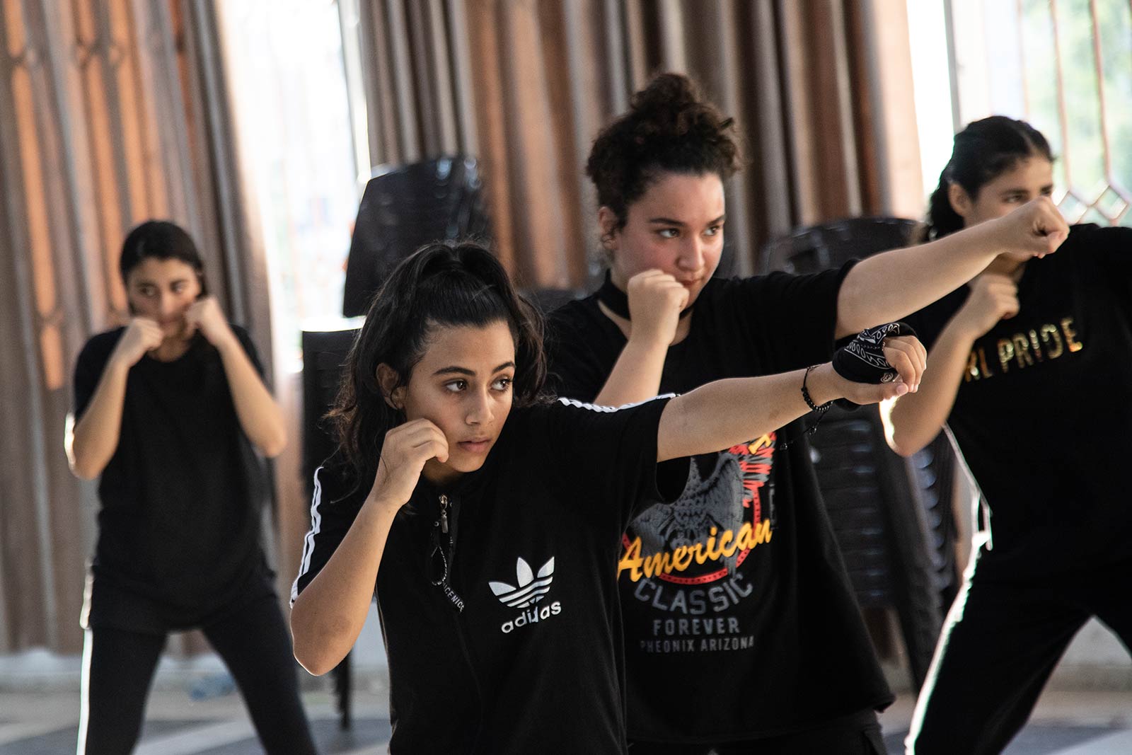 A row of young women keep their right fist to her cheek, holding out their left