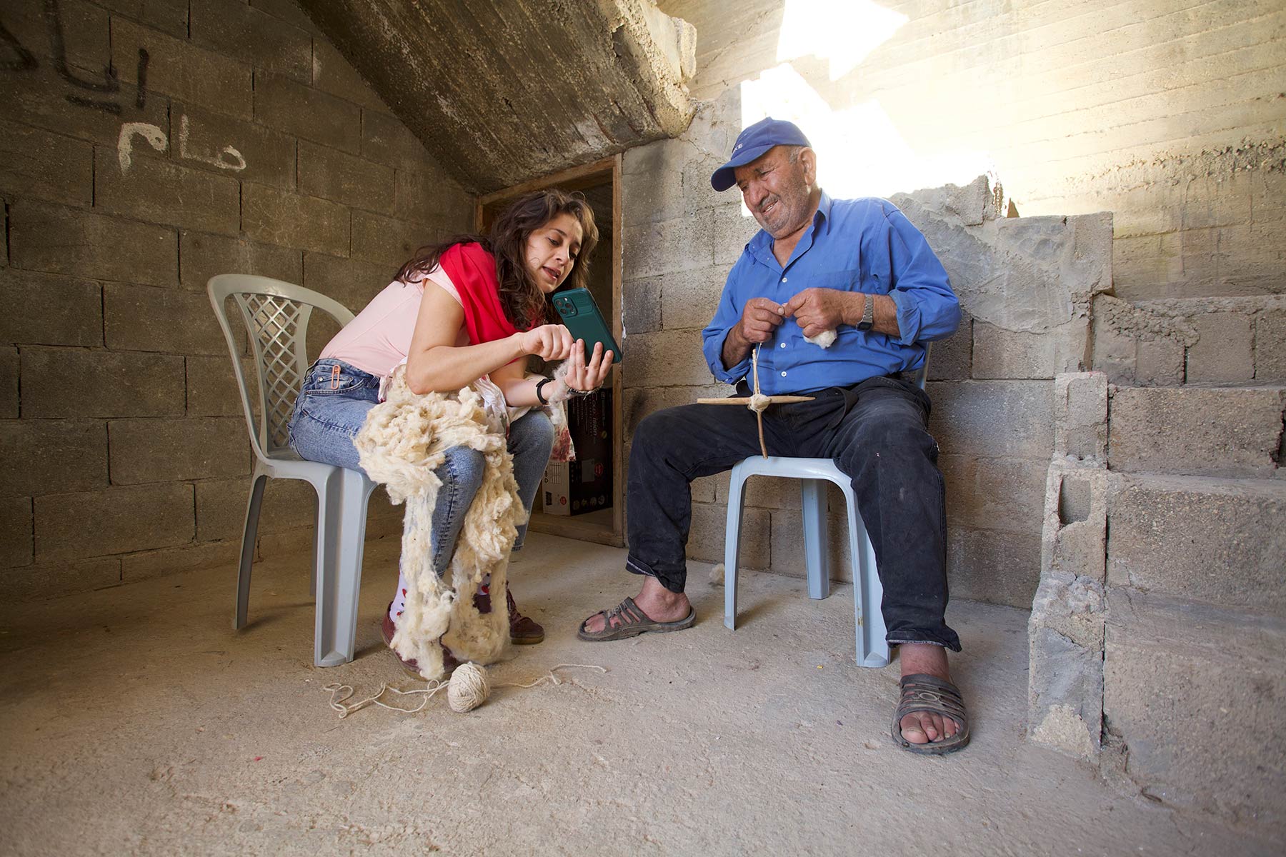 Lara Salous with shepherd Rajeh Al-Essa at his house in Mughayer village where he shows her how to use the Palestinian traditional drop spindle (Ghazzale)